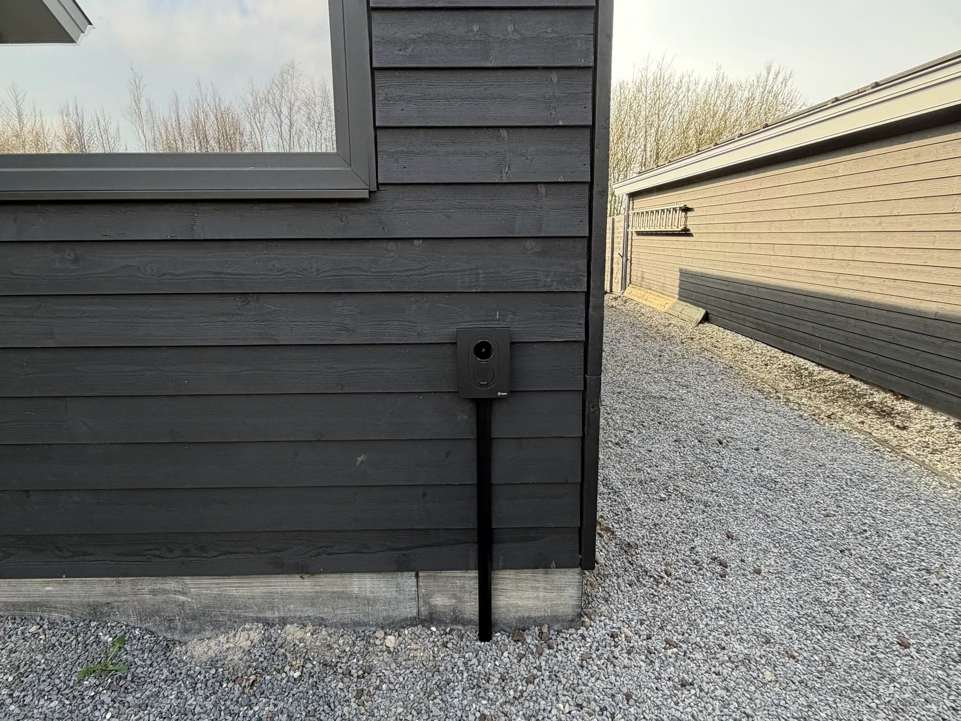 Een compact laadpunt tegen de donkere gevel, met de kabelroute langs de wand.